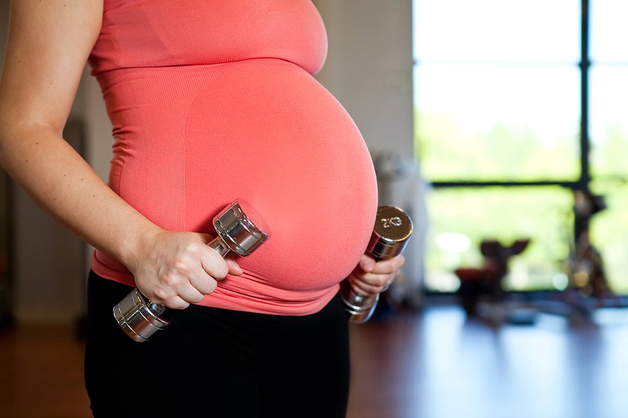 A pregnant woman holding dumbbells in a standing position in preparation for exercise